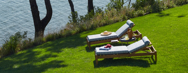 a pair of outdoor chaises on a grassy knoll near the ocean.