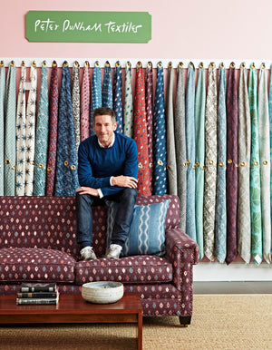 Peter Dunham sitting on the shoulder of a colorful sofa in front of colorful fabric samples
