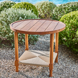 Round wooden side table with slatted top and woven lower shelf with cushions