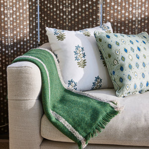 Upholstered sofa with beige upholstery, green throw blanket, patterned accent pillows