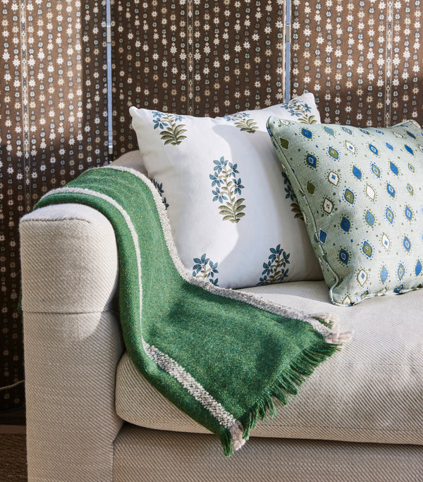 Upholstered sofa with beige upholstery, green throw blanket, patterned accent pillows