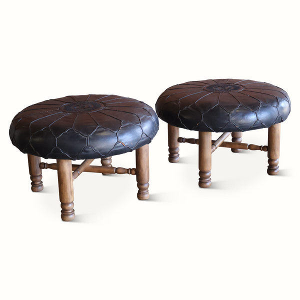Pair of round leather ottomans with dark brown tufted tops and wooden legs