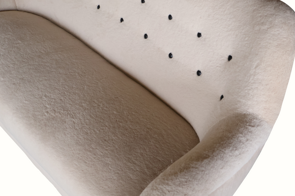 Close-up of light gray sofa upholstery with button-tufted back and smooth seat cushion.