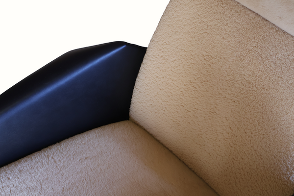 Lounge chair corner with dark leather armrest and beige sheepskin cushion, tight close-up