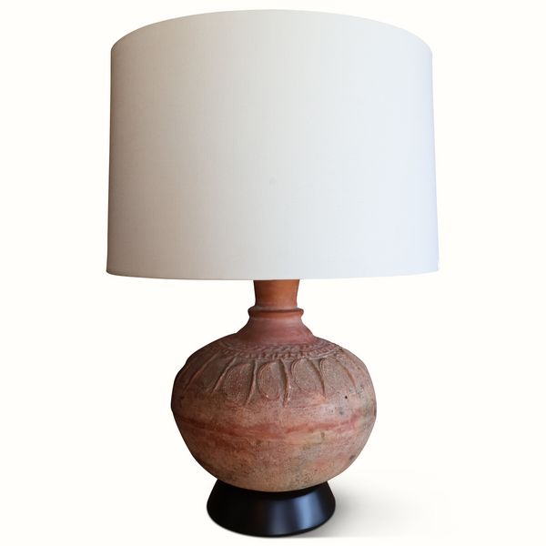 Pottery table lamp with rounded terracotta base, carved relief details, tan fabric shade
