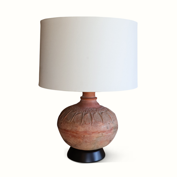 Pottery table lamp featuring a round terracotta ceramic base with carved motif and tan shade