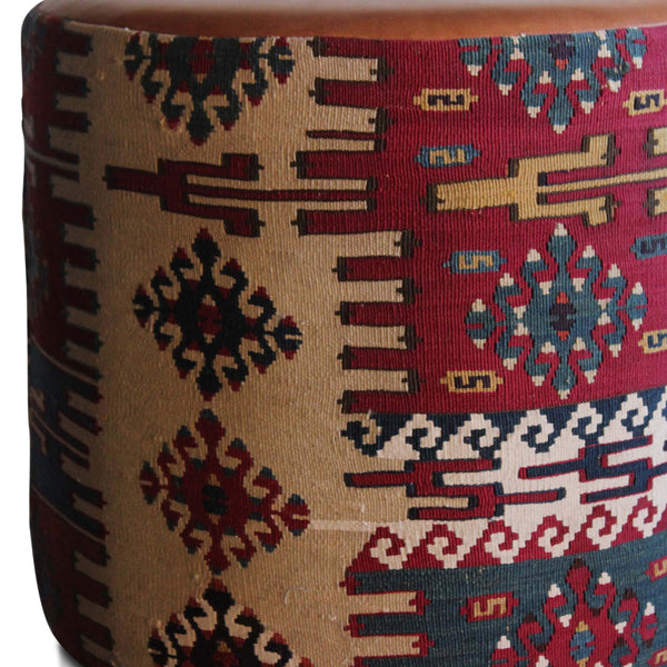 Kilim pouf side with geometric motifs in red, blue, cream, and brown; tan top edge