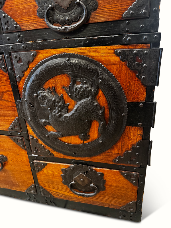 Wooden tansu chest drawer front with dragon relief knob and ornate metal trim.