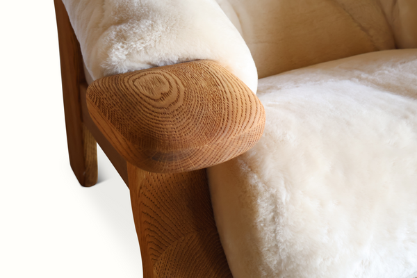 Oak armchair armrest with light sheepskin seat cushion and visible wood grain