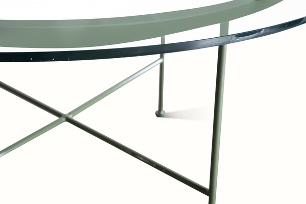 Green metal patio table side view with curved tabletop and diagonal cross brace