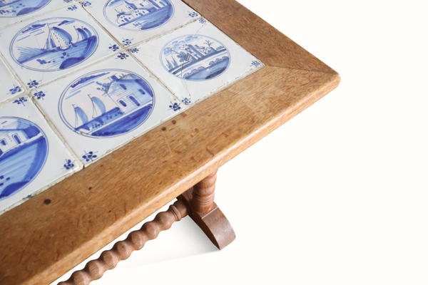 Close-up of blue-and-white Delft tile inset on wooden table corner with turned leg