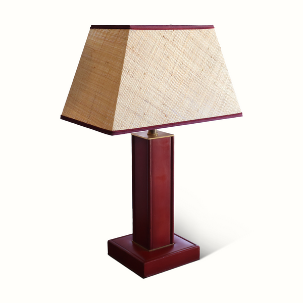 Red leather table lamp on square base, beige fabric shade with dark trim and brass.
