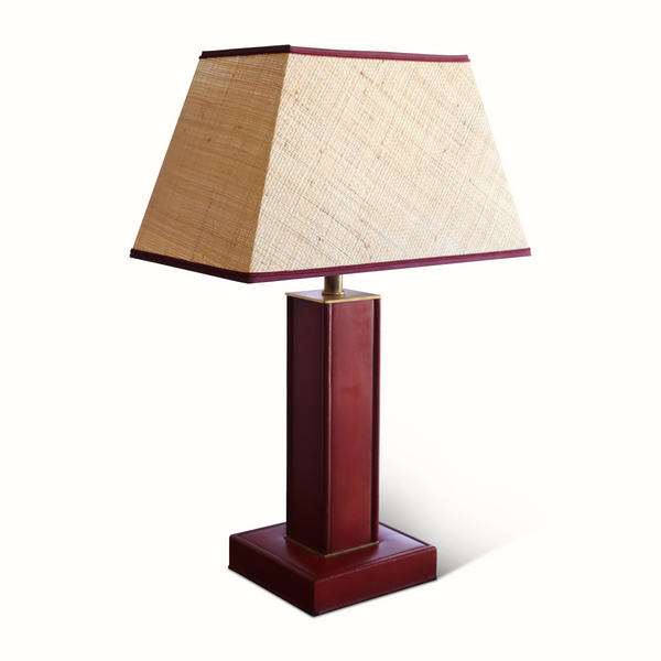 Red leather table lamp with tall column and square base, beige shade, brass top.