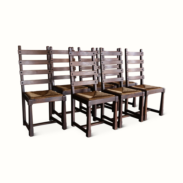 Set of seven oak ladderback chairs with woven beige cushions and dark wood legs.