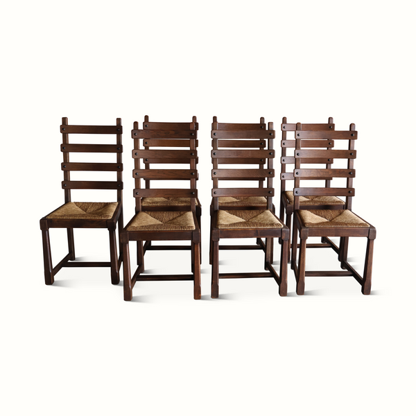 Set of seven oak ladderback chairs with woven beige seats and dark wood frames.