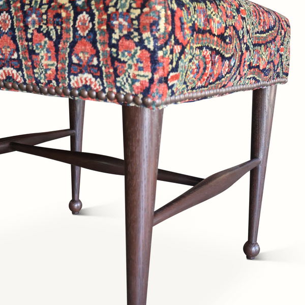 Single upholstered stool corner with patterned seat, turned legs, and nailhead trim