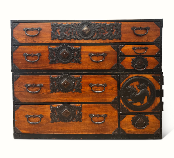 Wooden tansu chest with four drawers and decorative metal hardware, orange-brown wood.