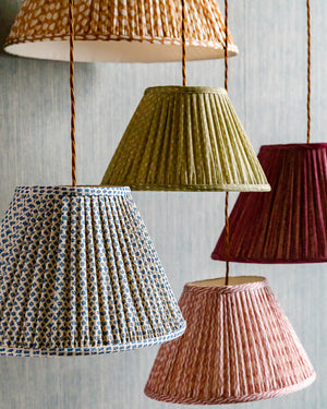 Hanging lampshades made from pleated, gathered printed fabrics, set against a gray-blue background
