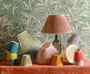 A cheerful array of patterned, gathered pleated lampshades against a patterned backdrop of green fabric. On an orange tablecloth.