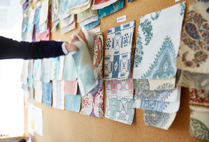 a cork board full of fabric samples with a hand holding a few, revealing motion
