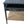 Black console table corner with woven paper rush shelf and metal drawer knob.