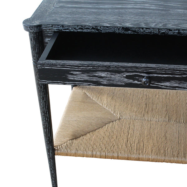 Black console table corner with woven paper rush shelf and metal drawer knob.